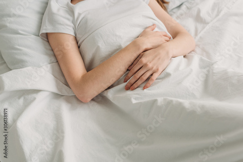 cropped view of woman lying in bed and suffering from stomach pain