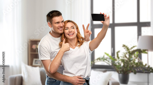 relationships, technology and people concept - happy couple in white t-shirts taking selfie smartphone and showing peace by over home background