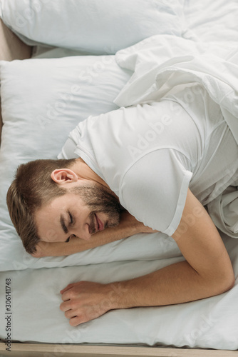 overhead view of young man smiling while sleeping on white bedding