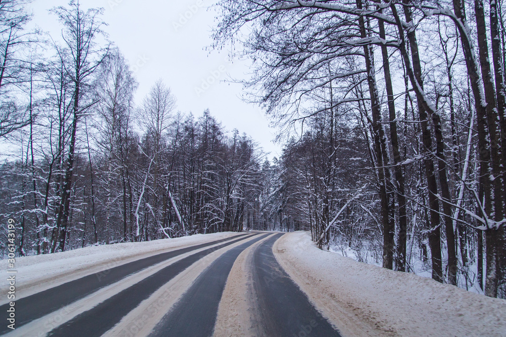 Obraz premium Asphalt road in the forest covered with snow