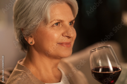 people, alcohol and drinks concept - close up of happy senior woman drinking red wine from glass at home in evening