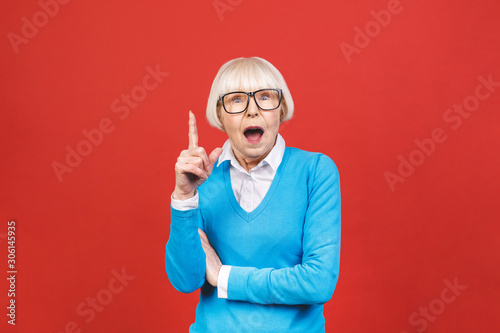 Senior happy aged businesswoman wearing glasses. Beautiful old woman has idea. Isolated on red background.