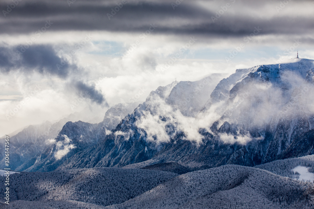 Beautiful mountain panorama in winter with fog and clouds. Bucegi mountains seen from Postavaru, Romania.