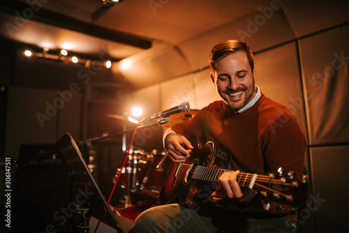 Portrait of a happy man playing guitar in the studio.