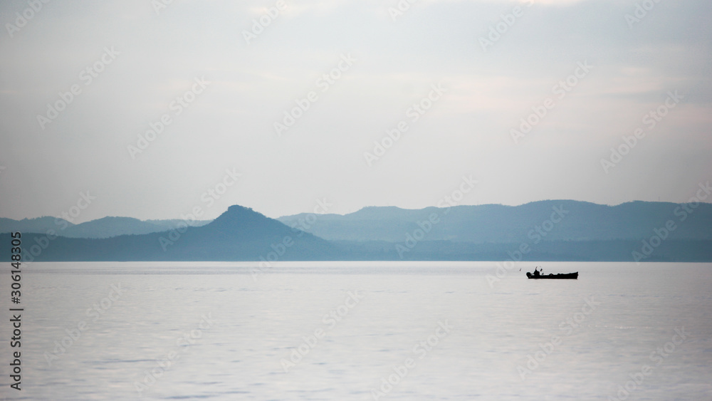 Lake Garda, Italy. A view of a solitary fisherman in his boat with a backdrop of the Italian Alps. Lake Garda, Italy. A view of a solitary fisherman in his boat with a backdrop of the Italian Alps.
