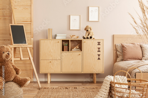 Stylish wooden commode with plush toy on top next to single bed in kid's bedroom