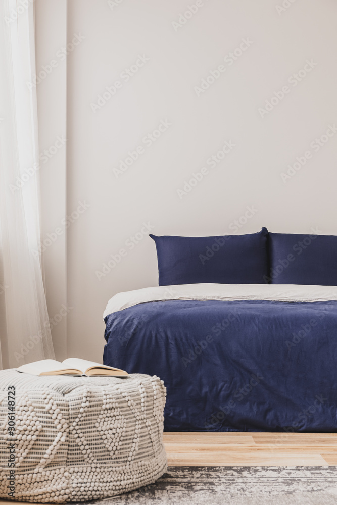 Empty bedroom interior with simple blue bed and book on pouf, copy space on the wall