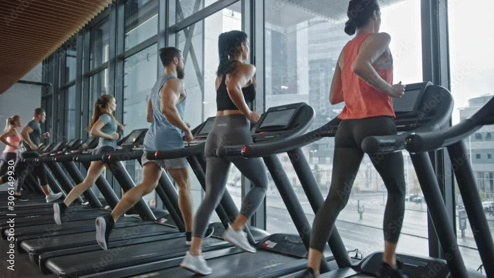 Group of Six Athletic People Running on Treadmills, Doing Fitness Exercise. Athletic People Actively Workout in the Modern Gym. Sports People Workout in Fitness Club. Side View Slow Motion
