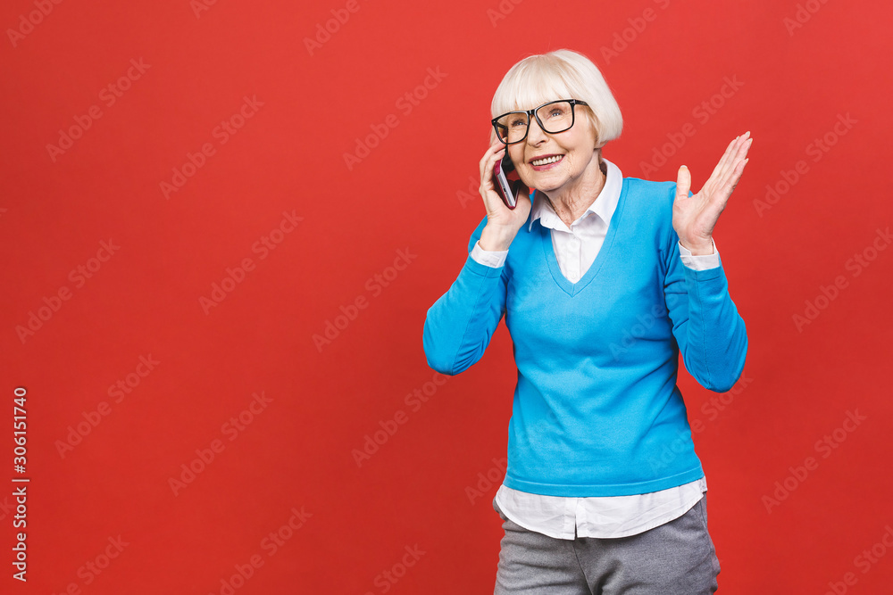 Fototapeta premium Phone conversation. Positive senior aged woman smiling while talking on the phone isolated over red background.