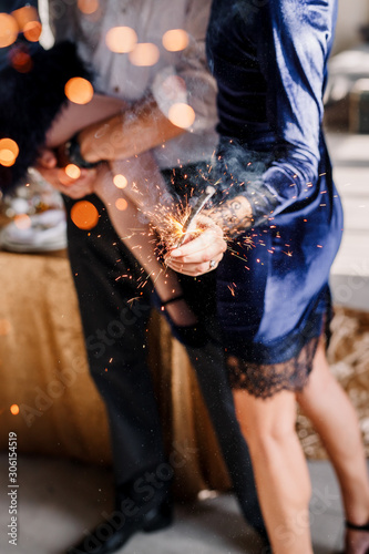 Happy family in blue - woman, man and little girl, with a sparkler in hand, near the New Year's table for Christmas at home. The girl at the father on hands. New year 2019.