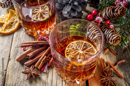 Fototapeta Naklejka Na Ścianę i Meble -  Christmas winter alcohol drink. Orange, spice and bourbon whiskey alcoholic cocktail in two glasses, wooden background with christmas tree branches and decor, copy space