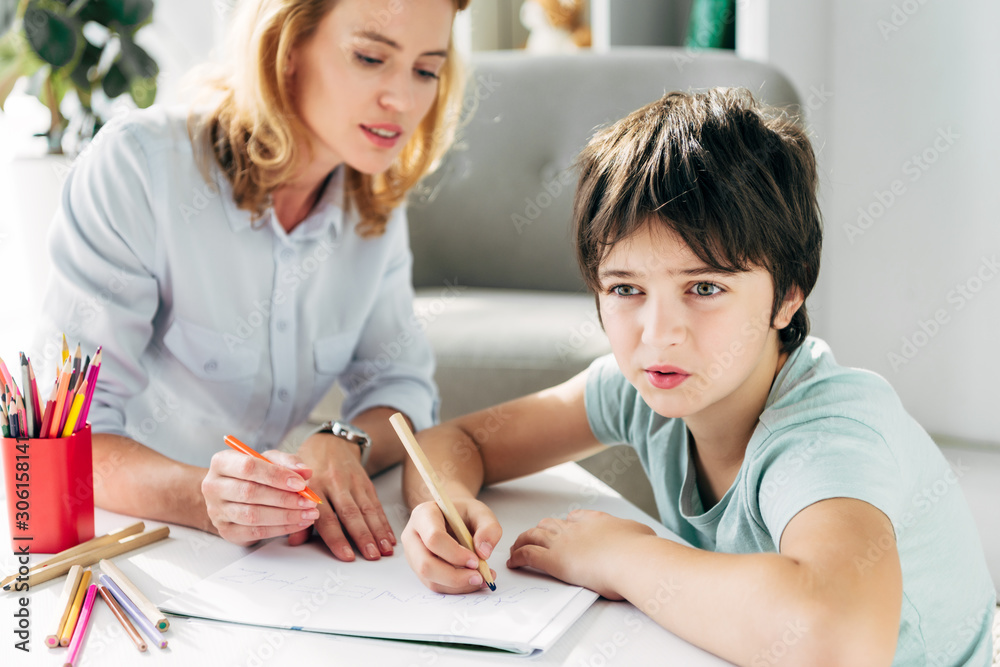 kid with dyslexia and child psychologist sitting at table and holding pencils