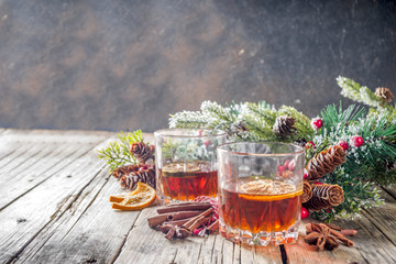 Christmas winter alcohol drink. Orange, spice and bourbon whiskey alcoholic cocktail in two glasses, wooden background with christmas tree branches and decor, copy space