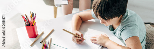 panoramic shot of kid with dyslexia drawing on paper with pencil photo