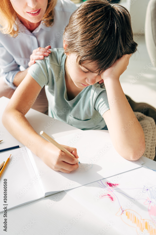cropped view of child psychologist and sad kid with dyslexia drawing with pencil cropped view of child psychologist and sad kid with dyslexia drawing with pencil