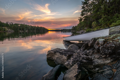 A lone canoe sits on shore on peaceful Eagle Lake at sunset. The odd colored clouds in the background are from a forest fire in Northwest Ontario, Canada in the summer of 2018. photo