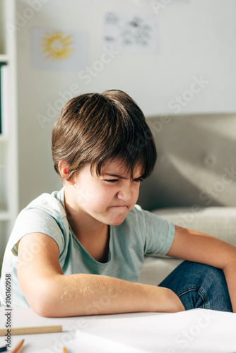 irritated kid with dyslexia sitting at table and looking away