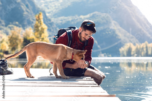 Young traveler hiker with backpack giving water to dog on the lake.