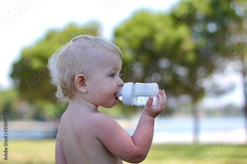 Little boy feeling thirsty and drinking water from a baby bottle. The baby is wearing a diaper.