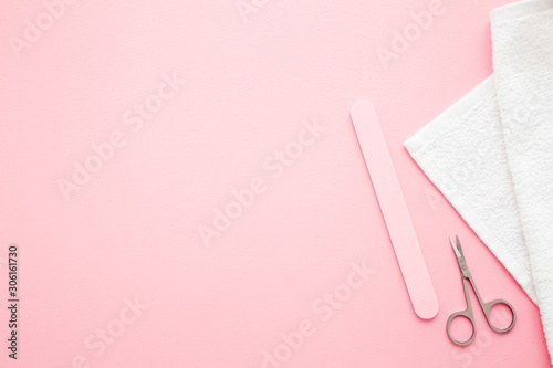Фотография Scissors, nails file and white towel on pastel pink table