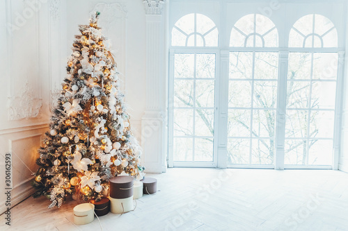 Classic christmas New Year decorated interior room New year tree. Christmas tree with gold decorations. Modern white classical style interior design apartment, large window. Christmas eve at home