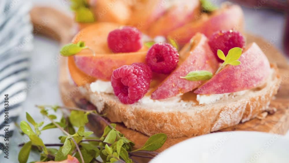 Peach ricotta toasts garnished with walnuts, fresh mint, and raspberries on a wooden cutting board. Peach ricotta toasts garnished with walnuts, fresh mint, and raspberries on a wooden cutting board.