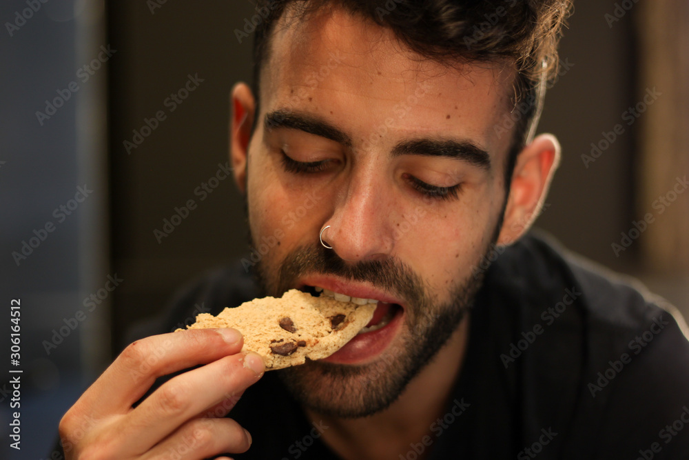 Young man with nose piercing eating chocolate cookie Young man with nose piercing eating chocolate cookie