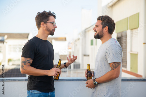 Photography Two male friends excited with discussion over bottle of beer on outdoor terrace