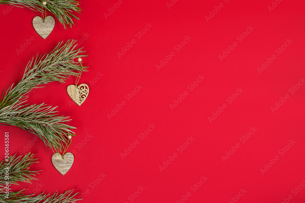A Christmas wooden homemade decor in the form of a hearts hanging on a pine branchs with hoarfrost. Flat lay on red background with copy space.