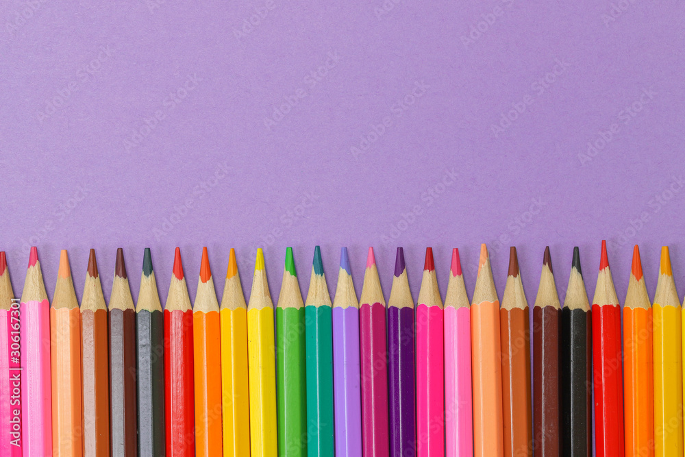 Close up row of colored pencils isolated against a purple background Close up row of colored pencils isolated against a purple background