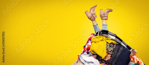 woman legs out of clothes pile on yellow background with copy space photo