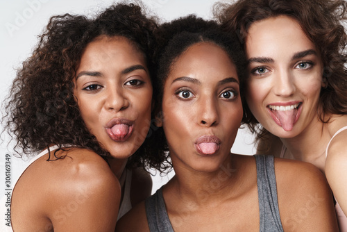 Portrait of three joyful multiracial women standing together and showing their tongues