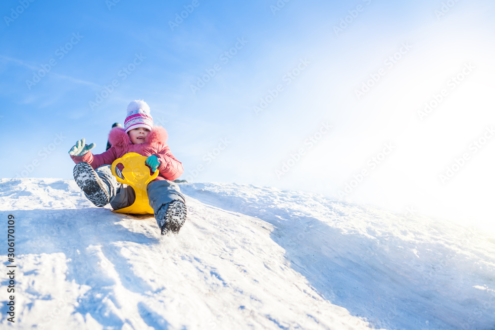 Happy small girl in winter clothing riding downhill