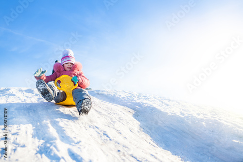 Happy small girl in winter clothing riding downhill