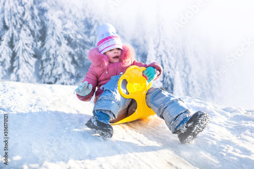 Happy small girl in winter clothing riding downhill on snow with winter