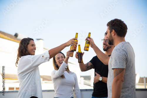 Happy excited friends celebrating great event and toasting beer on outdoor terrace. Young men and women in casual meeting outside. Celebration or party concept