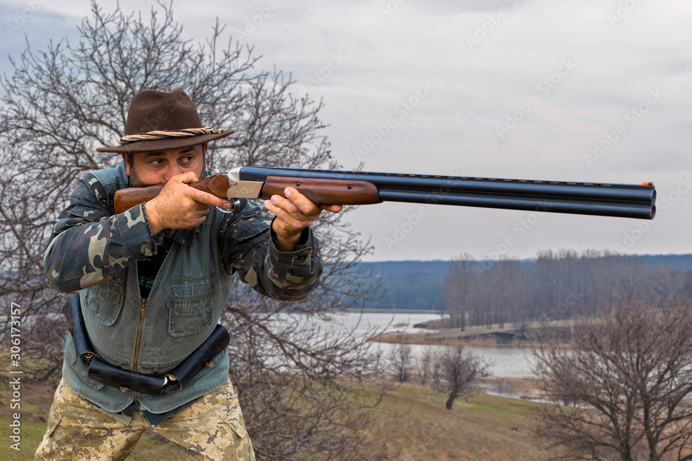 Fototapeta premium Hunting period, autumn season open. A hunter with a gun in his hands in hunting clothes in the autumn forest in search of a trophy. A man stands with weapons and hunting dogs tracking down the game...
