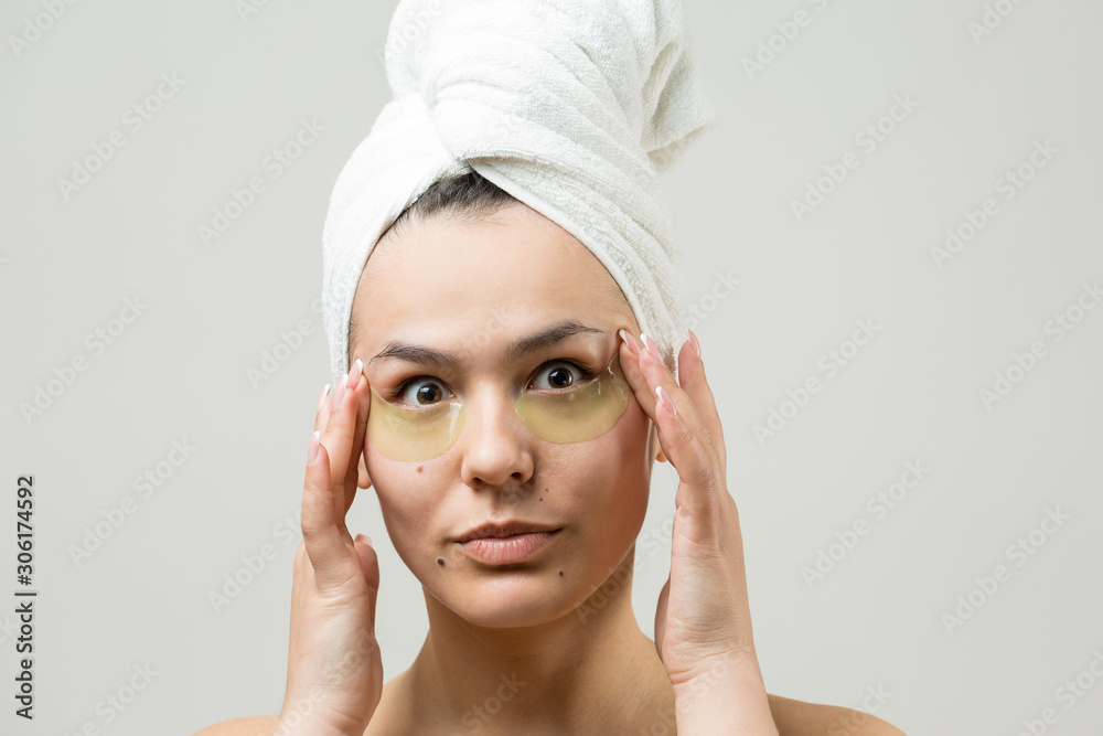 Young beautiful girl in a white towel on his head wears collagen gel patches under her eyes. Mask under eyes treatment face.