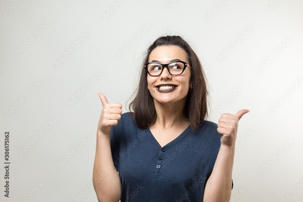 Happy young caucasian female with glasses and a blue T-shirt making thumb up sign and smiling. Good job and respect. Happy young caucasian female with glasses and a blue T-shirt making thumb up sign and smiling. Good job and respect.