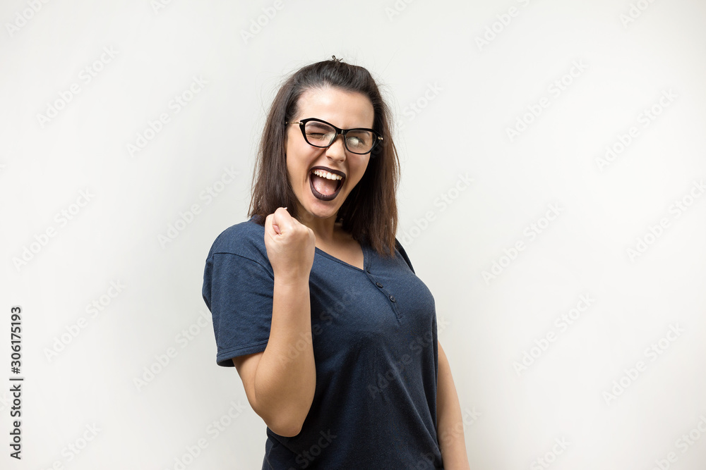 Happy young caucasian femalein in a blue shirt with glasses lifts a clenched fist up for joy. Success and happiness of the work. Successful person, victory! Happy young caucasian femalein in a blue shirt with glasses lifts a clenched fist up for joy. Success and happiness of the work. Successful person, victory!