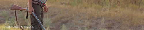 Hunter with a hat and a gun in search of prey in the steppe, Aims for prey. Panoramic image for your text, toned.