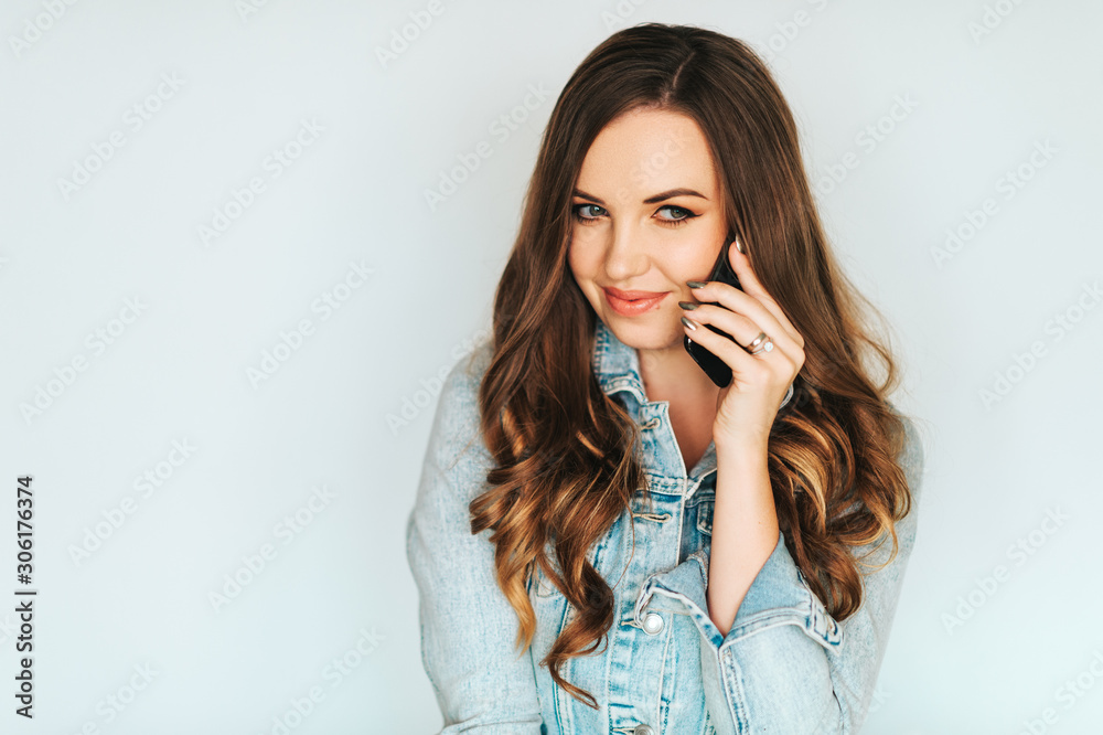 Portrait of young beautiful woman with long hairstyle, wearing blue denim jacket, talking on the phone