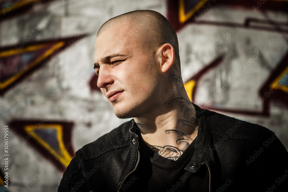 Bald tattooed young brutal guy with a tattoo on his neck. Young handsome  guy in a black denim jacket and a black t-shirt. Close-up, face, portrait  of an attractive young man. Stock