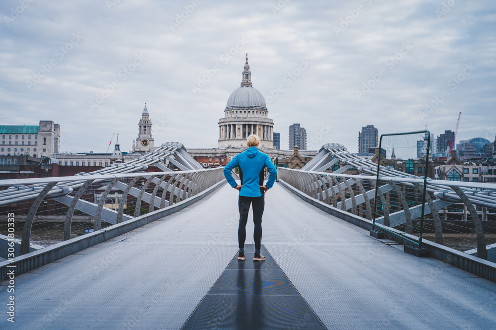 Young active man standing at Millennium Footbridge over the Thames and looking at St Paul's Cathedral