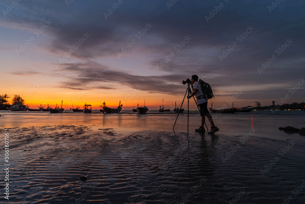 An Asian man stood to take pictures. Sea and boat in the evening when the sun goes down