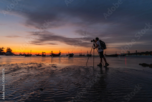 An Asian man stood to take pictures. Sea and boat in the evening when the sun goes down