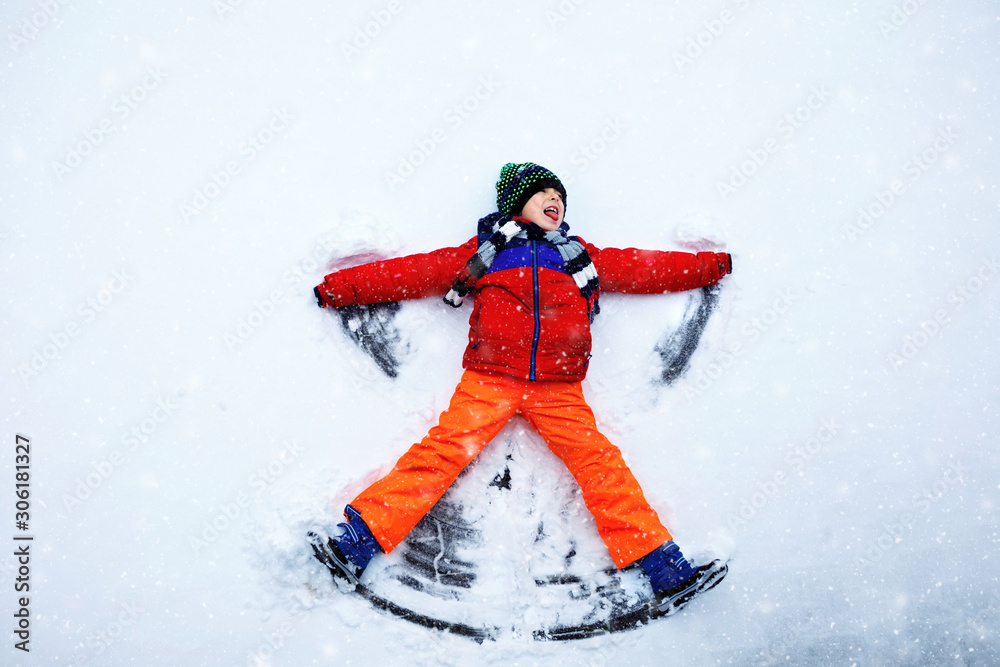 Cute little kid boy in colorful winter clothes making snow angel, laying down on snow. Active outdoors leisure with children in winter. Happy healthy child having fun and laughing outdoors