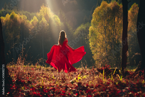 Beautiful brunette girl in a chic red dress posing in the fairy autumn forest.