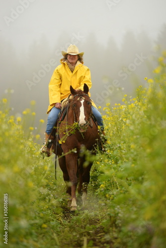 flowers for the ladies. Reiterin im gelben Regenmantel reitet durch gelbe Blumen