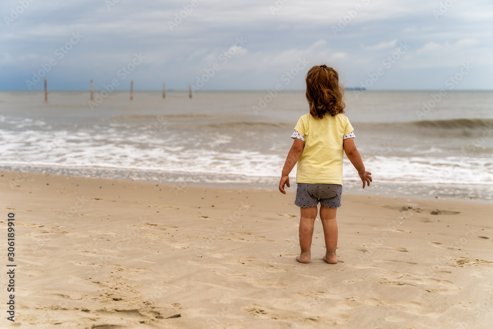 kleines Kind allein am Strand bei wolkigem Wetter